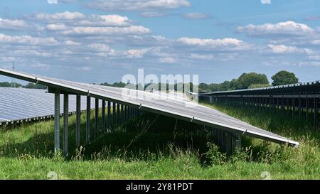 a large solar energy farm featuring rows of photovoltaic panels solar energy farm in full sunlight in a rural area with trees and blue skies. Renewabl Stock Photo