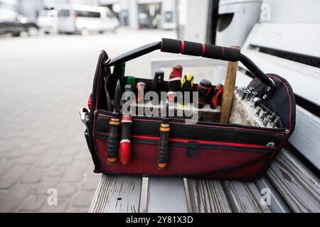 A well-organized tool bag filled with various hand tools including screwdrivers and pliers, placed on a wooden bench in a sunny outdoor environment. Stock Photo