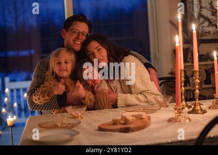 A family enjoys a cozy dinner by candlelight, smiling and embracing each other at a festively decorated table. Stock Photo