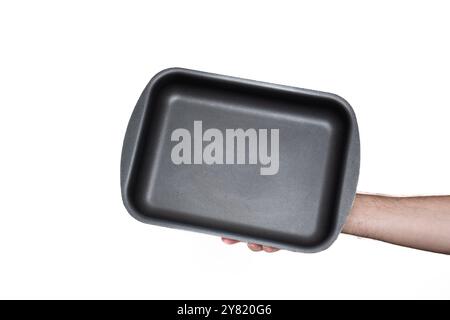 Empty, black, rectangular deep baking tray or casserole. Held by hand by Caucasian male hand. Close up studio shot, isolated on white. Stock Photo