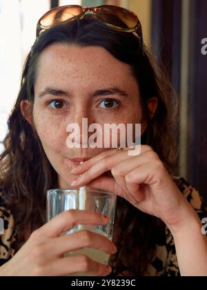 A woman with freckles and brown hair sipping a drink through a straw, wearing a leopard print top and round sunglasses perched on her head. Stock Photo