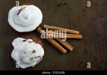 Top View of Cinnamon Buns with White Icing and Cinnamon Sticks on Baking Sheet Horizontal Stock Photo