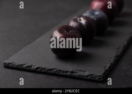 Juicy ripe fresh plum with water drops on black slate board. Seasonal fruit on black background. Selective focus, close-up. Stock Photo
