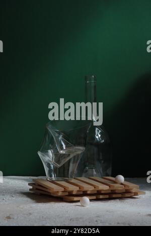 Empty wine glass and tumblers on a wooden board, tilted diagonally on a stone, set against a white-green background for a dynamic, minimalist display Stock Photo