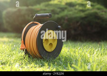 One extension cord reel on green grass outdoors, space for text Stock Photo