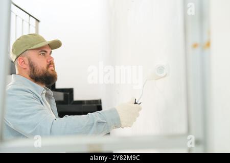 View through a stepladder on a man in construction gloves painting a wall  Stock Photo