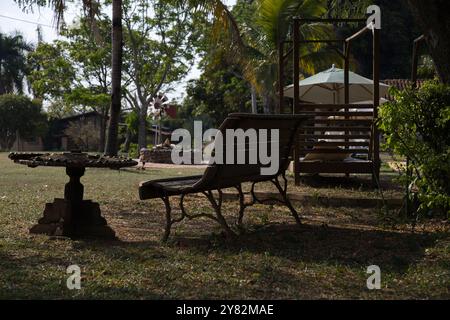 A wooden bench sits in a park with a table nearby. The bench is empty and the table is covered in leaves. The scene is peaceful and quiet, with the on Stock Photo