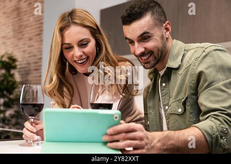 Smiling man and woman using digital tablet in the kitchen. Happy carefree couple planing together with online device and a drink at home. Stock Photo