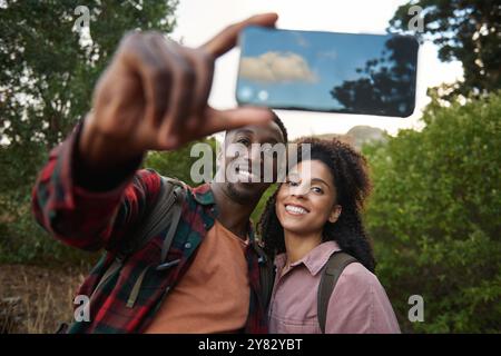 Portrait of young multiethnic couple smiling and taking a smartphone selfie together while out for a hike in some rugged hills in the summertime Stock Photo