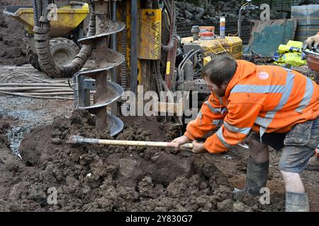 Man manually clearing of spoils from auger pile drilling machine drilling hole in clay soil on domestic construction site Stock Photo