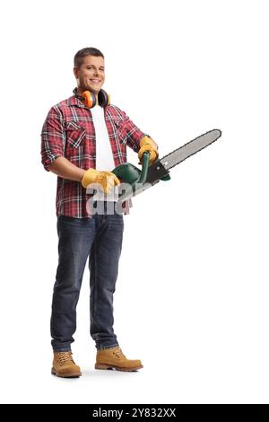 Full length portrait of a young man holding a chainsaw and smiling isolated on blue background Stock Photo