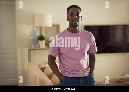 Portrait of a young African man smiling while standing with his hands in his pockets in his living room at home Stock Photo