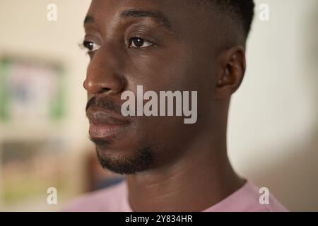 Close-up of a young African man standing alone at home and looking deep in thought Stock Photo