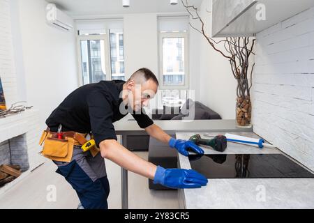 craftsman installs hob in kitchen. Household Appliance Installation Services Concept Stock Photo