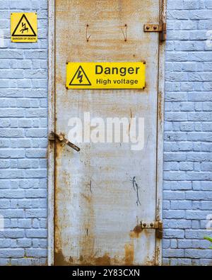 Rusty door with a high voltage danger sign, white bricks wall. Stock Photo