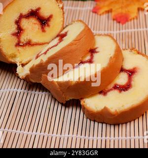 Rolled Cake Slices on Bamboo Mat. Close up of several pieces of rolled cake with red jam inside, arranged on a bamboo stand. Stock Photo