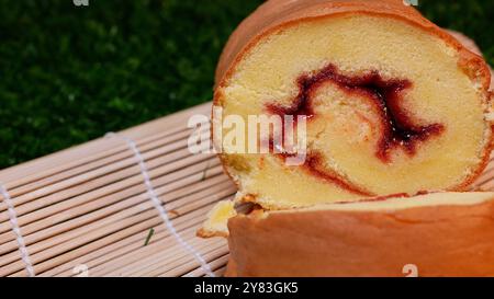 Rolled Cake Slices on Bamboo Mat. Close up of several pieces of rolled cake with red jam inside, arranged on a bamboo stand. Stock Photo