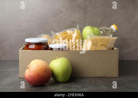 Different food products for donation in box on grey table Stock Photo