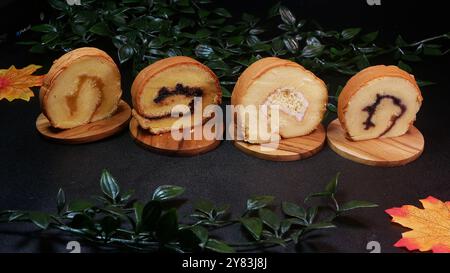 Four soft slices of rolled cake with different fillings, ranging from fruit jam to nut cream, served on wooden boards with a background of green leave Stock Photo