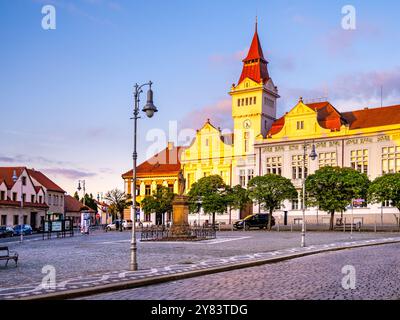 The historic Town Hall stands proud in Marianske Square at dusk, illuminated by warm evening light. Nearby, charming buildings and vibrant greenery create a picturesque atmosphere. Stock Photo