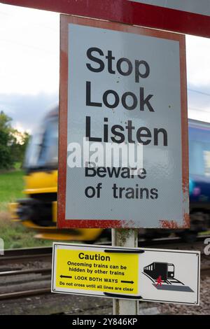 Northern Trains train passing Stop Look Listen sign at pedistrian crossing, Burley in Wharfedale, Ilkley, Leeds, West Yorkshire Stock Photo