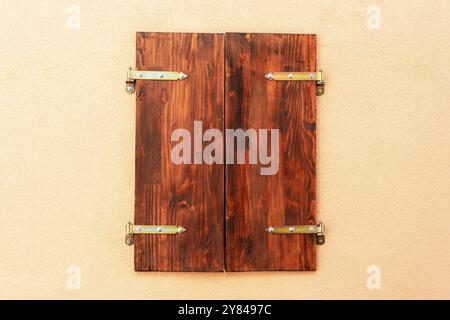 Closed window with wooden shutters on beige wall. Stock Photo