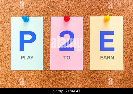 Conceptual 3 letters keyword P2E (Play To Earn), on multicolored stickers attached to a cork board. Stock Photo