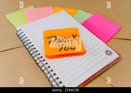Thank you phrase written on recycled cardboard with a background of a lined notebook and post-it notes Stock Photo
