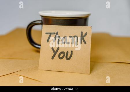 Phrase of gratitude written on a recycled cardboard with a cup of black coffee on the background of a notebook. Stock Photo