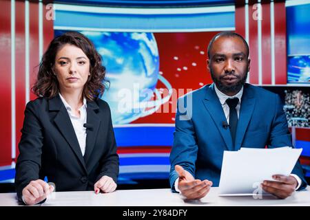 Diverse reporters doing newscast live on television broadcast, hosting morning show in newsroom. Two journalists talking about media topics with latest information from headlines. Stock Photo