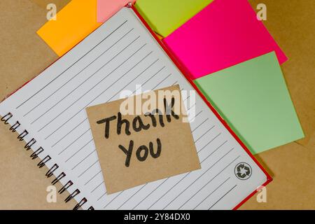 Thank you phrase written on recycled cardboard with a background of a lined notebook and post-it notes Stock Photo