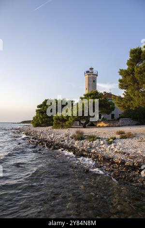 Beautiful sunset in a landscape on a rocky coast with a prominent lighthouse and pine forest. View over the coast to the building, on the Mediterranea Stock Photo