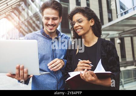 Two smiling colleagues are chatting in the street during lunch break near the building in the background Stock Photo