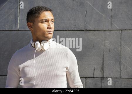 Serious Latin man with headphones on a gray wall background Stock Photo