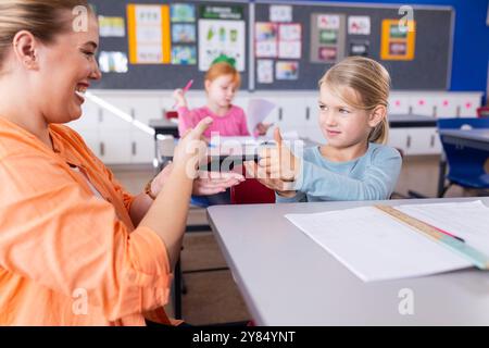 Practicing sign language, female teacher and student in school classroom, smiling together Stock Photo