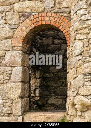 Roman arch in wall of old Cornish tin mine engine house constructed from red brick and Cornish granite, Botallack, Land’s End, Cornwall, England, UK. Stock Photo