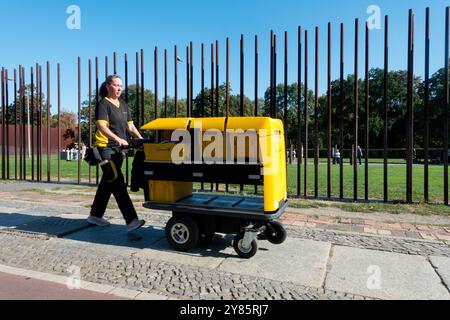 Deutsche Post office delivery woman with electric cart trolley walking along Berlin Wall Memorial Gedenkstätte Berliner Mauer Bernauer Straße Street Stock Photo