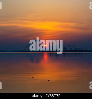 A serene sunset over calm waters in Oido, with warm colors reflecting on the still surface as the sun dips below the horizon. Stock Photo