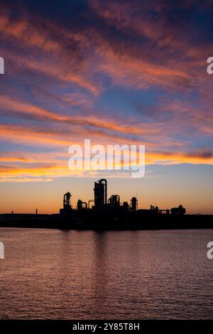 A stunning sunset over Bukseong Port in Incheon, where the silhouettes of industrial structures beautifully contrast with warm hues in the sky. Stock Photo