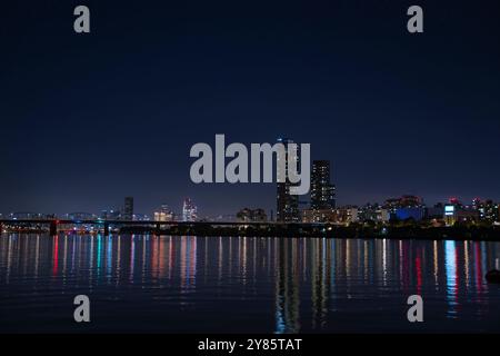 This photo shows the calm night view of the Han River, with city lights and skyscrapers shining in the distance, along with the bridge. Stock Photo