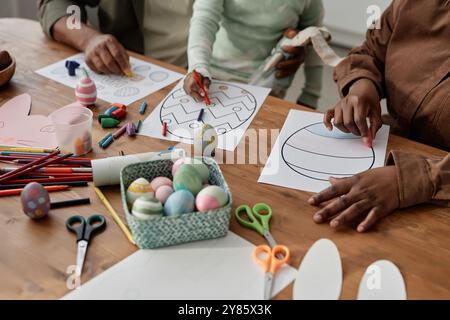 Adults and children creating hand-painted Easter eggs and colorful drawings on paper, surrounded with art supplies and decorated eggs without using natural light Stock Photo