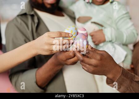Group of people holding brightly decorated Easter eggs in hands, sharing moment together, with soft-focus festive atmosphere visible in background Stock Photo