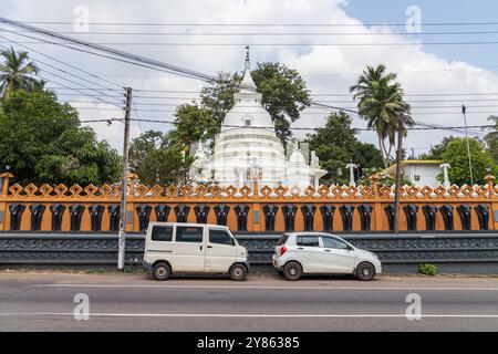 Malabe, Sri Lanka - December 4, 2021: Street view with parked cars. Dome of the Sri Sudharshanarama Purana Viharaya are on the background, this is the Stock Photo