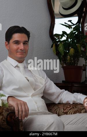 Handsome young man in a white shirt and tie sitting in a classic armchair next to the mirror where a hat is reflected, Spain Stock Photo