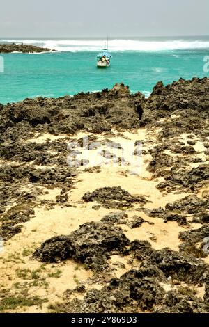 Rocky beach in a background of a fishing boat on the coastal water of Pero in Pero Batang, Kodi, Southwest Sumba, East Nusa Tenggara, Indonesia. Stock Photo