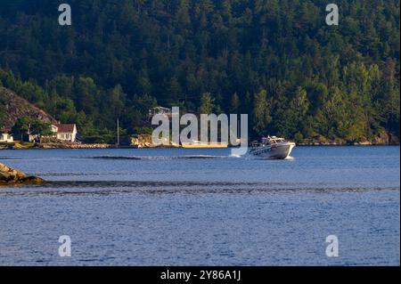 A taxi boat speeds across the water with Gumøy island and summer houses as a backdrop in the Kragerø archipelago in Telemark county, Norway. Stock Photo