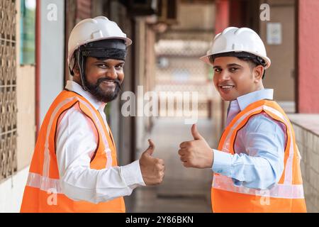 Two happy construction workers give a thumbs up at the construction site, symbolizing satisfaction, reliability, and trust in employee satisfaction. Stock Photo