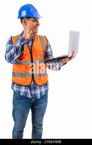 vertical smiling construction worker dressed in an orange safety vest and hard hat is engaged in video call using his laptop, white background. image Stock Photo