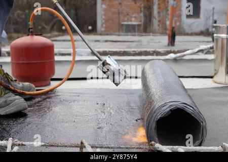 Laying and installing of rolled bituminous waterproofing membrane on concrete slab of house construction site. Professional workers heating and Stock Photo