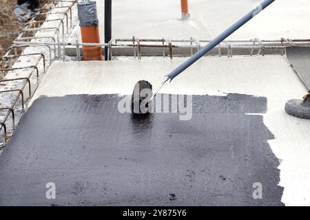 Worker applying a bituminous primer on a concrete slab at a construction site before laying bituminous waterproofing Stock Photo